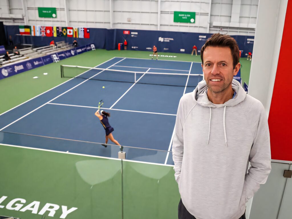 Daniel Nestor coaching tennis player serving on blue hard court in bright indoor facility with flags Wallpaper