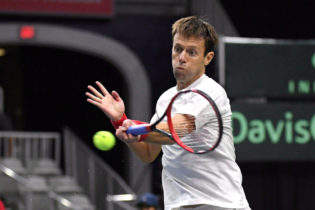 Daniel Nestor mid-swing intense Davis Cup tennis match dynamic motion green white court background Wallpaper