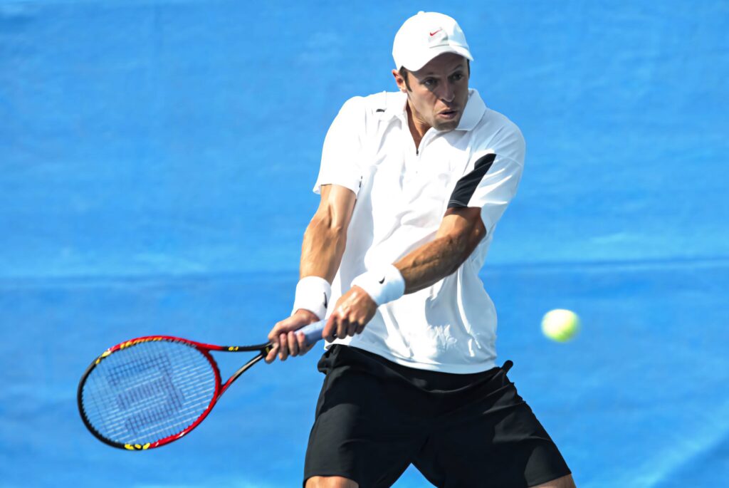 Daniel Nestor executing powerful two-handed backhand on vibrant blue tennis court in action shot Wallpaper