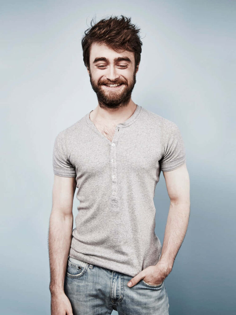 Daniel Radcliffe in casual grey henley and jeans smiling against soft blue gradient background Wallpaper