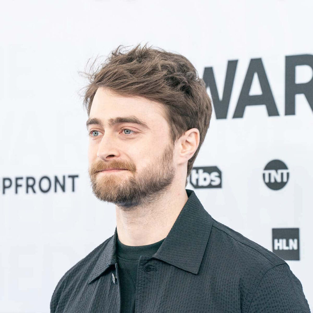 Daniel Radcliffe in dark textured jacket against white background with calm expression and beard Wallpaper