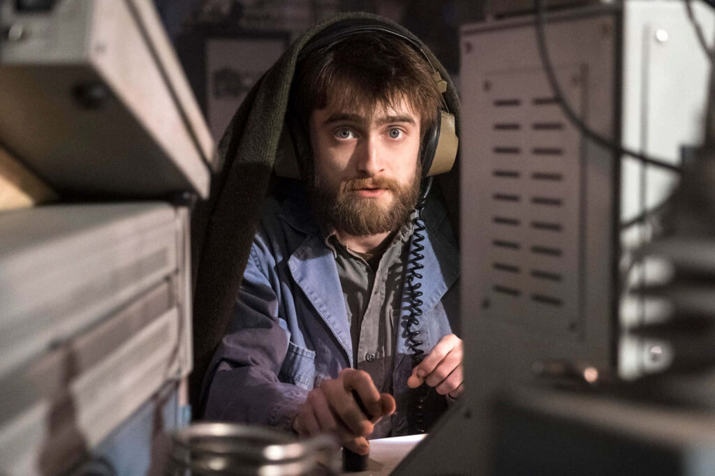 Daniel Radcliffe focused with headphones operating vintage radio equipment in dimly lit room Wallpaper