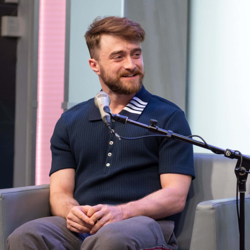 Daniel Radcliffe smiling in navy shirt in modern studio with soft lighting and sleek décor wallpaper background