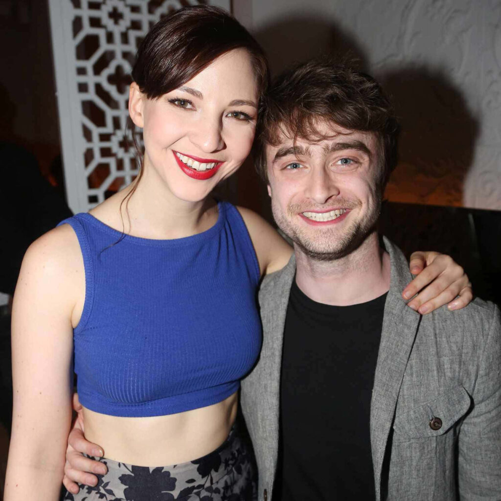 Daniel Radcliffe and Erin Darke smiling at event with elegant lighting and stylish backdrop Wallpaper