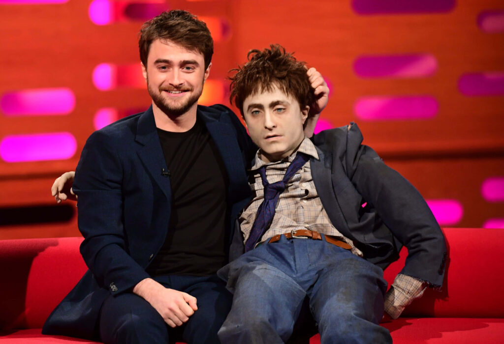 Daniel Radcliffe smiling on The Graham Norton Show with Swiss Army Man model under red pink lights Wallpaper