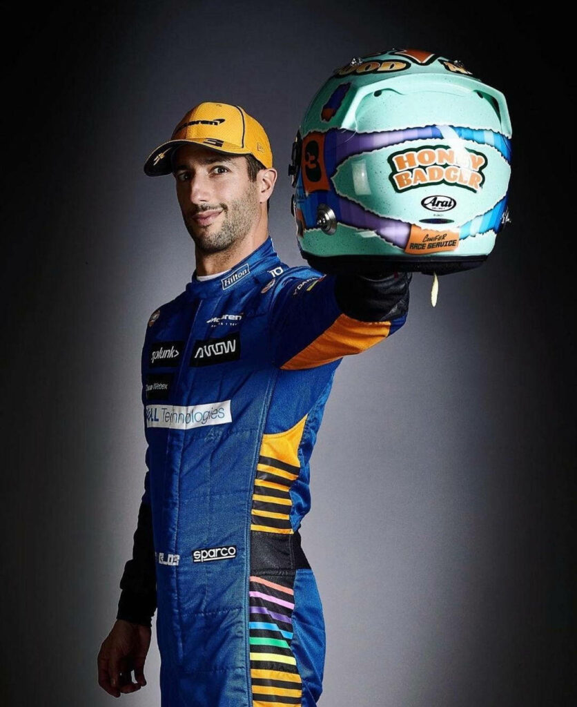 Daniel Ricciardo in vibrant blue orange racing suit holding colorful helmet studio background F1 star Wallpaper