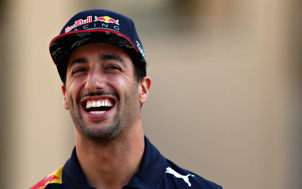 Daniel Ricciardo laughing in Red Bull Racing cap and shirt vibrant wallpaper background