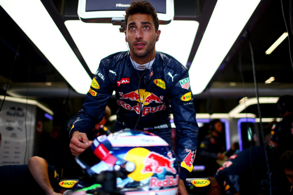 Daniel Ricciardo in Red Bull Racing suit with earphones in F1 garage vibrant focused scene Wallpaper
