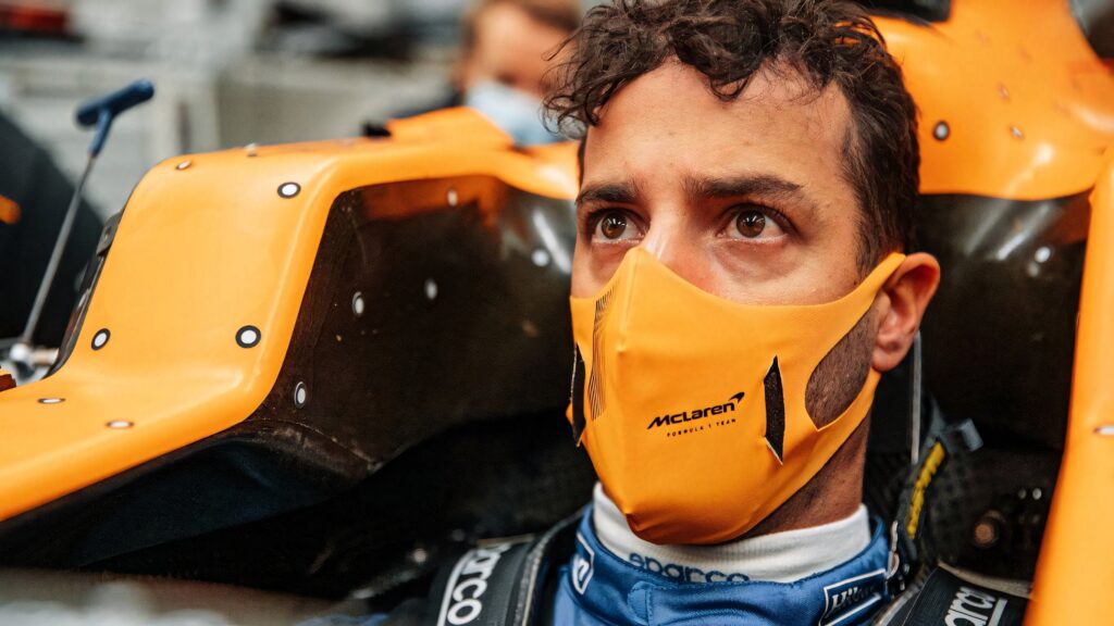 Daniel Ricciardo focused in bright orange McLaren F1 car wearing team mask and race suit wallpaper