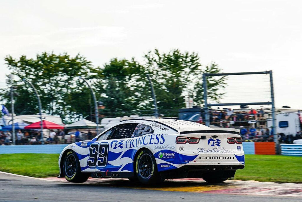 White Chevrolet Camaro race car number 99 driven by Daniel Suarez with blue graphics on track Wallpaper