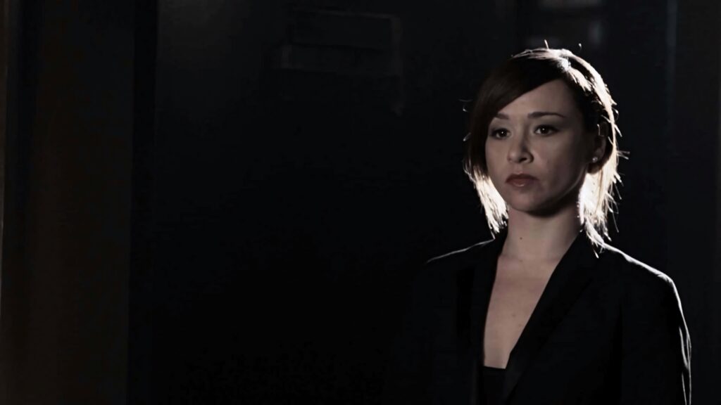 Danielle Harris in dark blazer standing in dimly lit room with dramatic cinematic shadows wallpaper