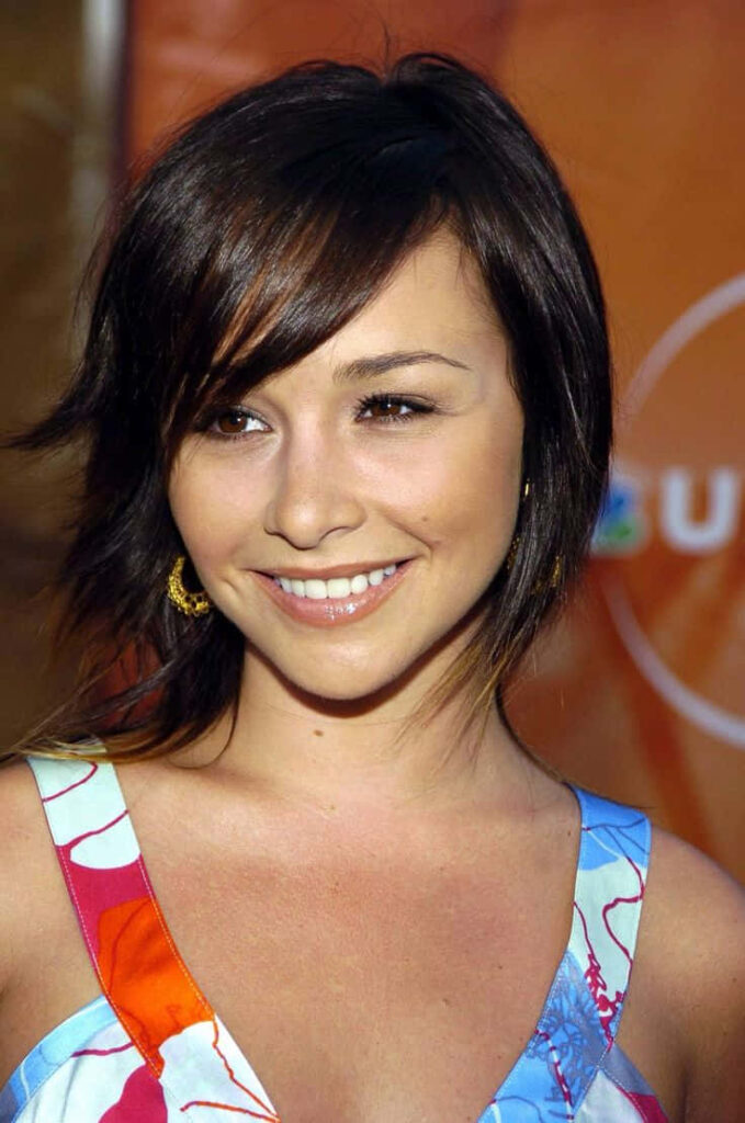 Danielle Harris smiling in colorful dress with layered bangs against warm orange wallpaper background