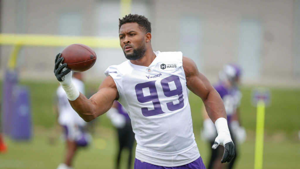 Danielle Hunter in Minnesota Vikings number 99 uniform catches football during outdoor practice Wallpaper