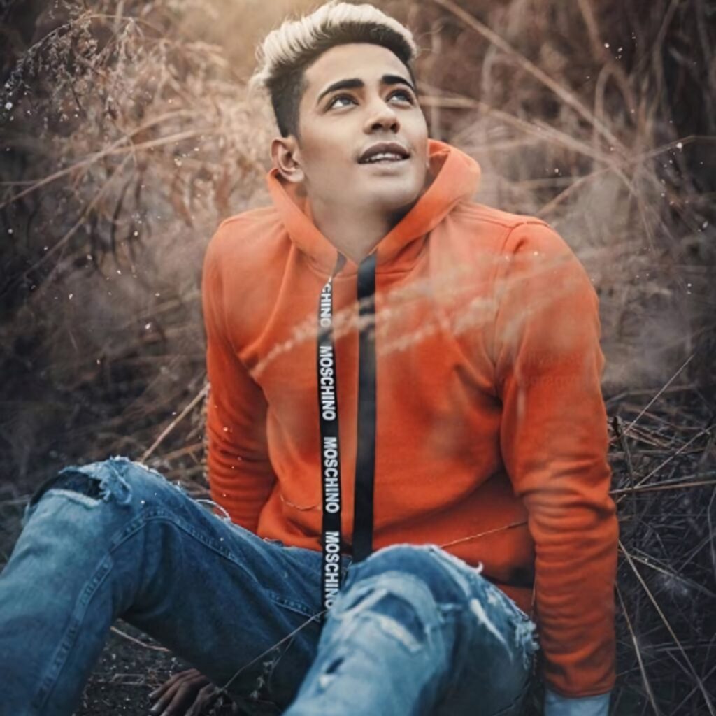 Danish Zehen outdoors in orange hoodie and ripped jeans surrounded by tall dry grass sunlight Wallpaper