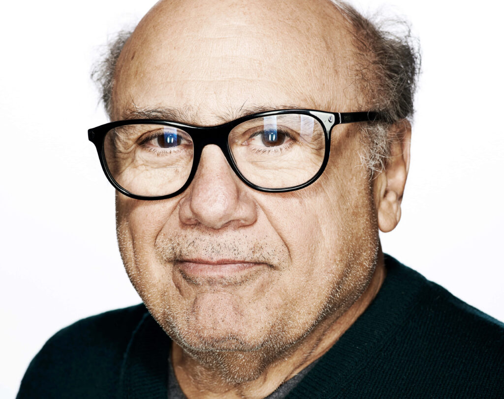 Close-up portrait of Danny DeVito with signature glasses warm expression white background wallpaper