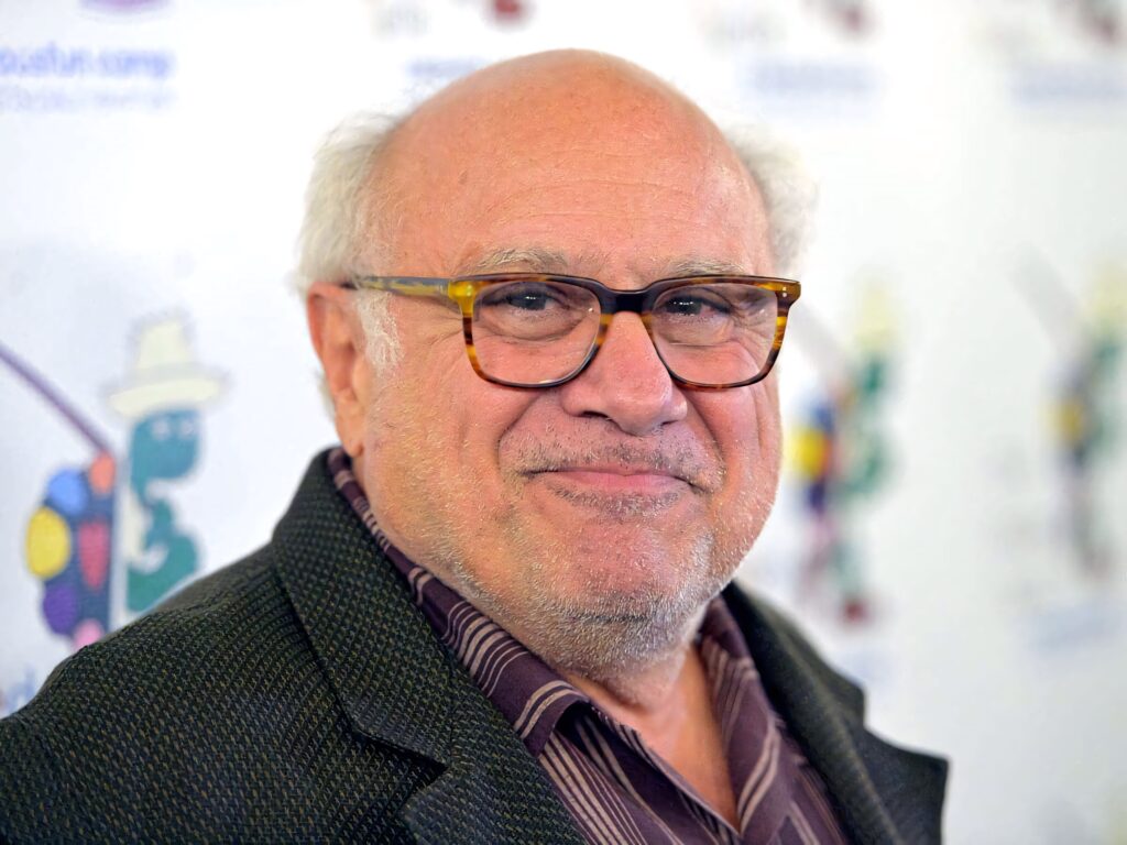 Close-up portrait of Danny Devito with signature glasses warm smile soft lighting wallpaper background