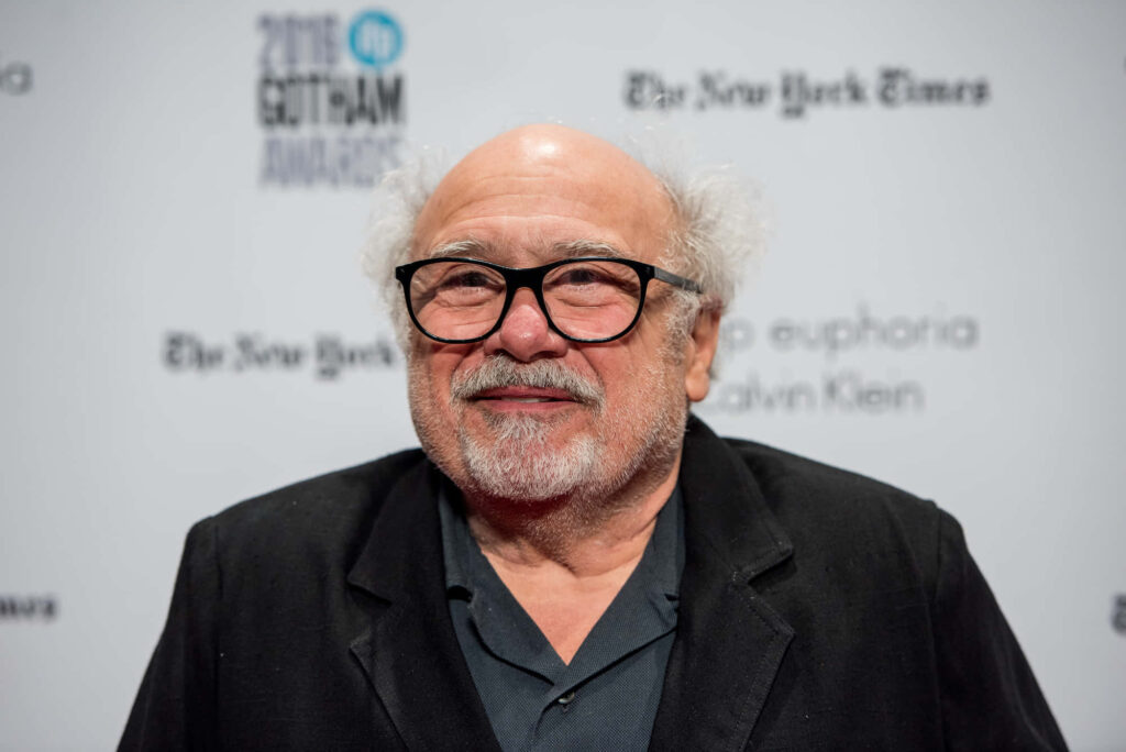 Danny Devito candid portrait wearing dark blazer and signature glasses on clean branded background Wallpaper
