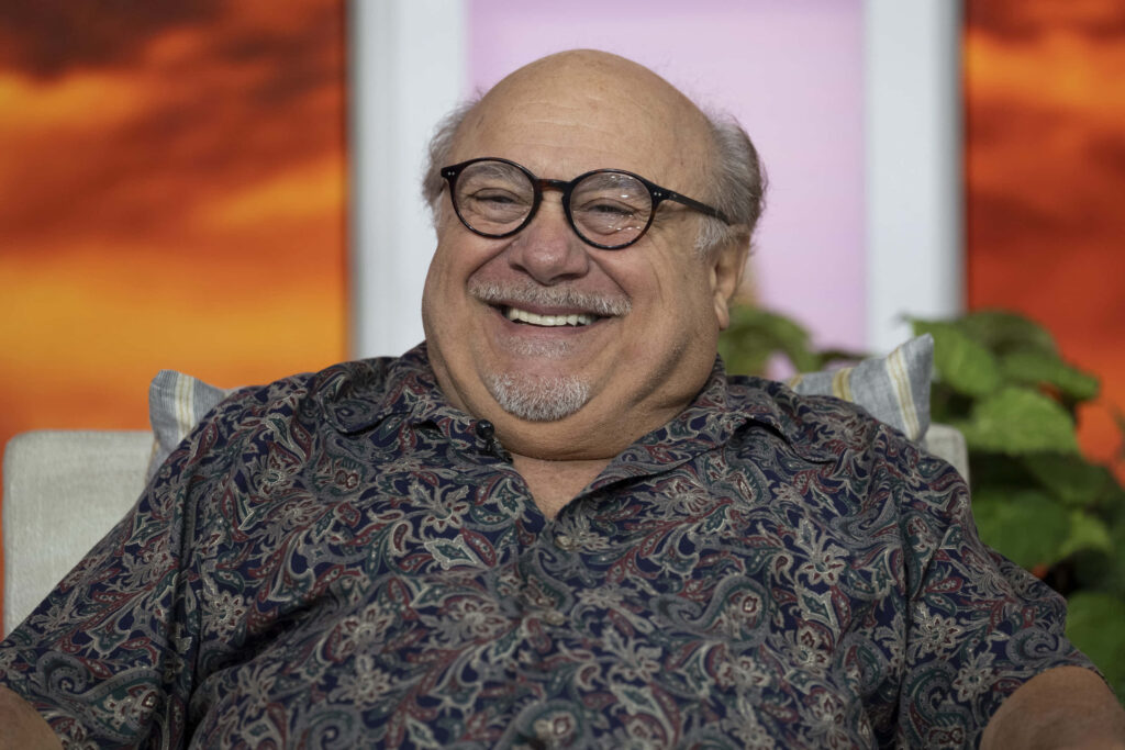 Danny Devito smiling warmly in sunset background with vibrant orange purple tones wallpaper