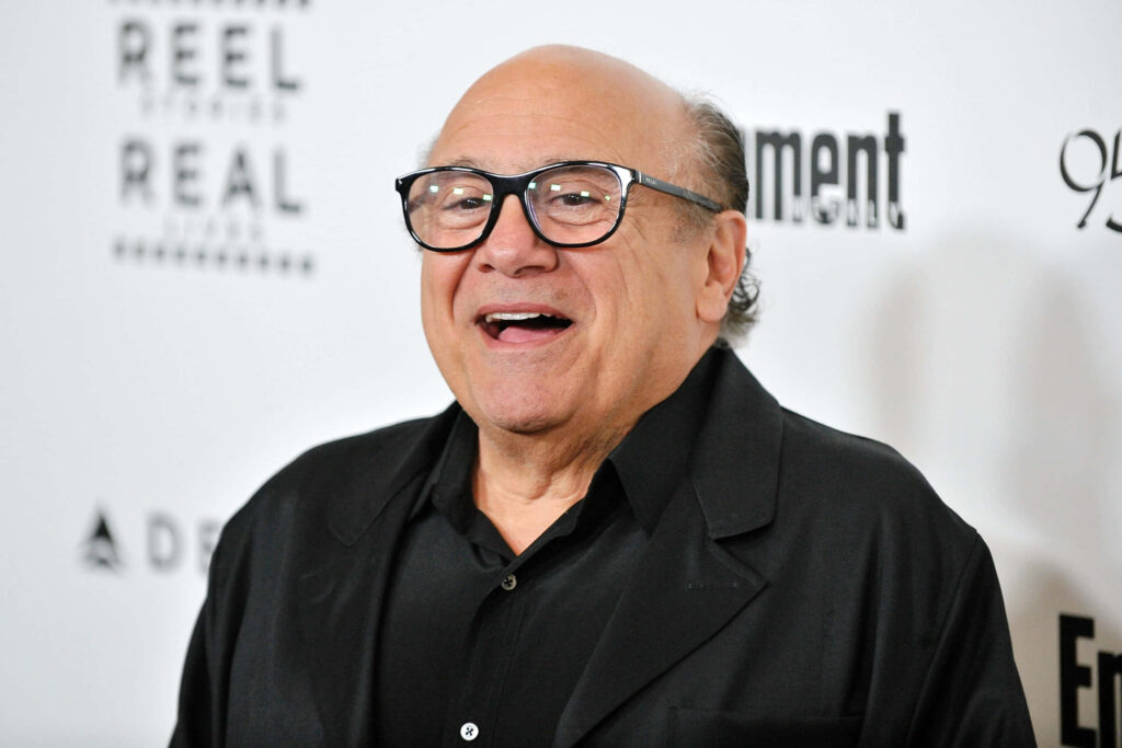 Danny Devito smiling in dark suit black glasses clean white background high-resolution portrait Wallpaper