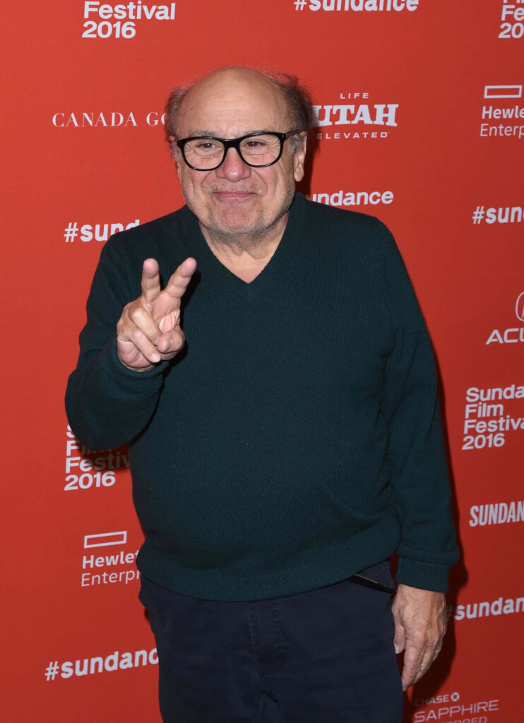 Danny Devito smiling and making peace sign at vibrant red Sundance Film Festival 2016 backdrop Wallpaper
