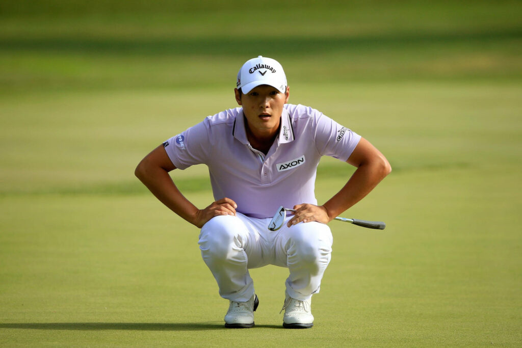 Danny Lee focused on green wearing white cap and sportswear on lush golf course background Wallpaper