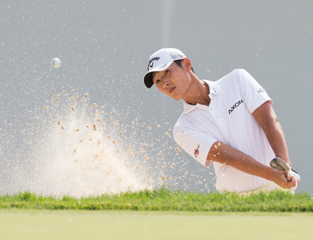 Danny Lee mid-swing chipping golf ball from sand bunker with flying sand and focused expression Wallpaper