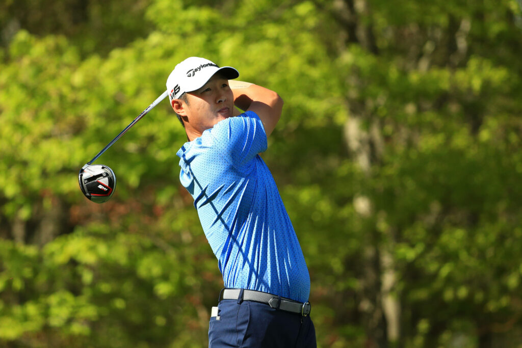 Danny Lee mid golf swing on green course wearing blue polo and white hat with sunlight filtering Wallpaper