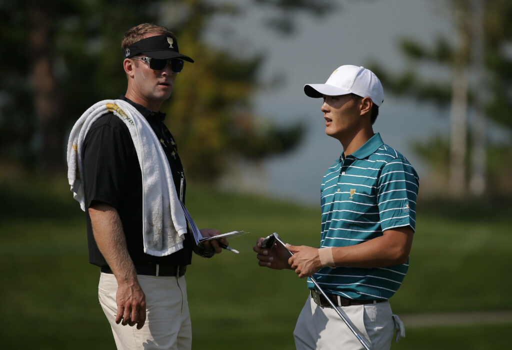 Danny Lee and coach Drew Steckel discuss golf strategy on sunlit lush green course in casual wear Wallpaper