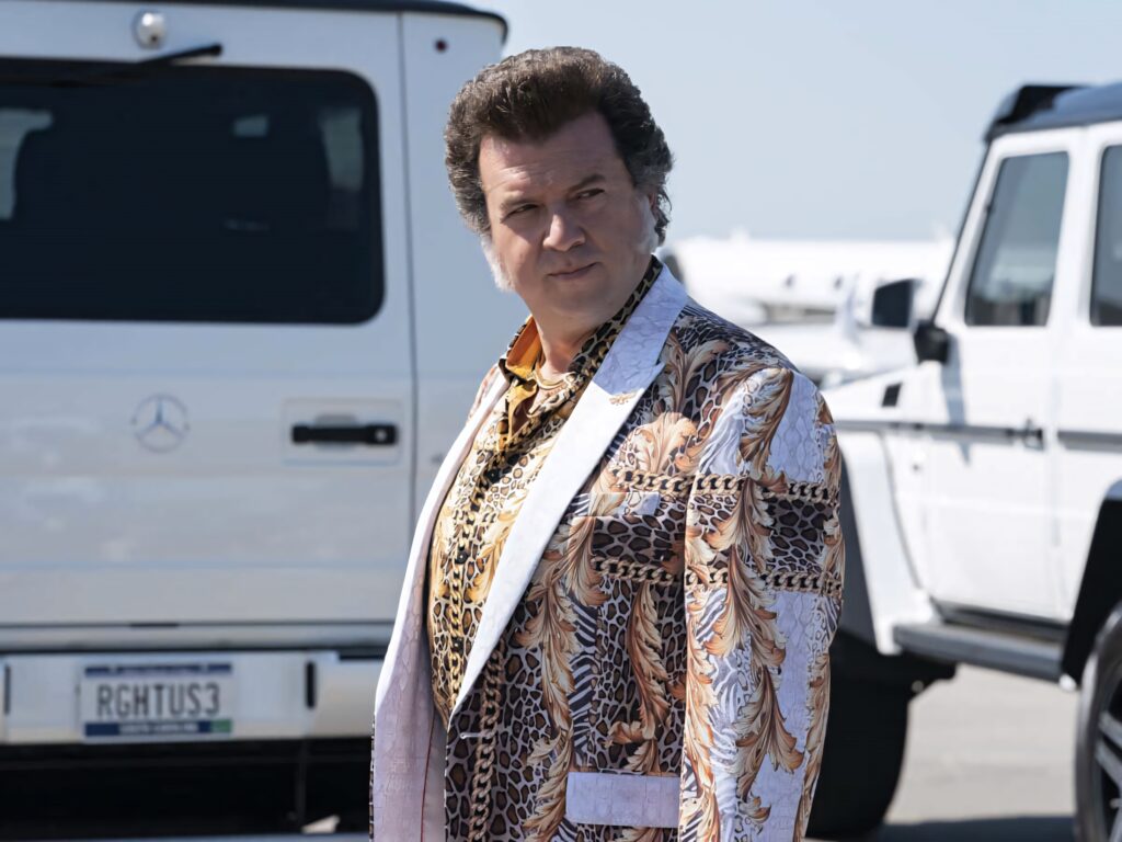 Danny McBride in bold patterned suit by luxury white cars bright daylight vibrant stylish wallpaper