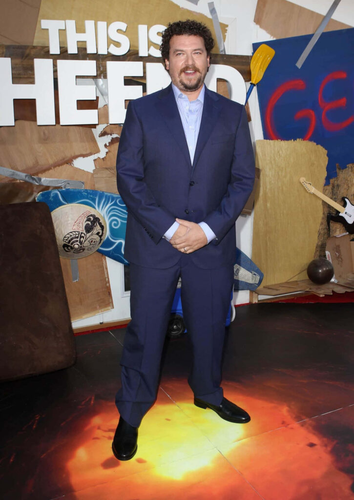 Danny McBride in navy suit with eclectic cardboard textured background and bold text wallpaper