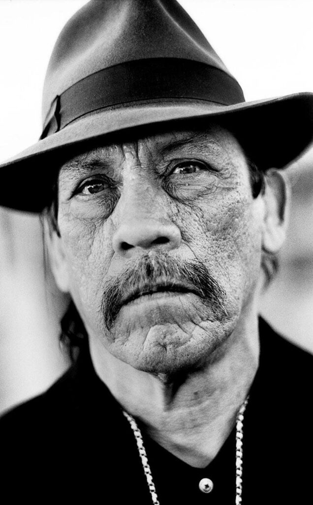 Black and white portrait of Danny Trejo with fedora and chain emphasizing rugged intense gaze Wallpaper