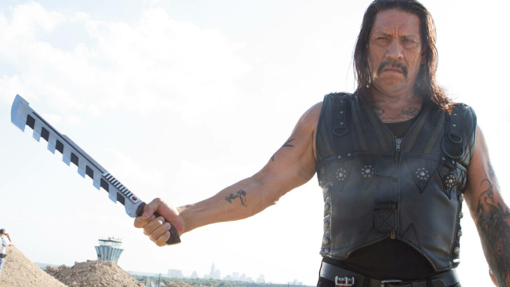 Danny Trejo in leather vest holding machete against bright sky action wallpaper Machete Kills