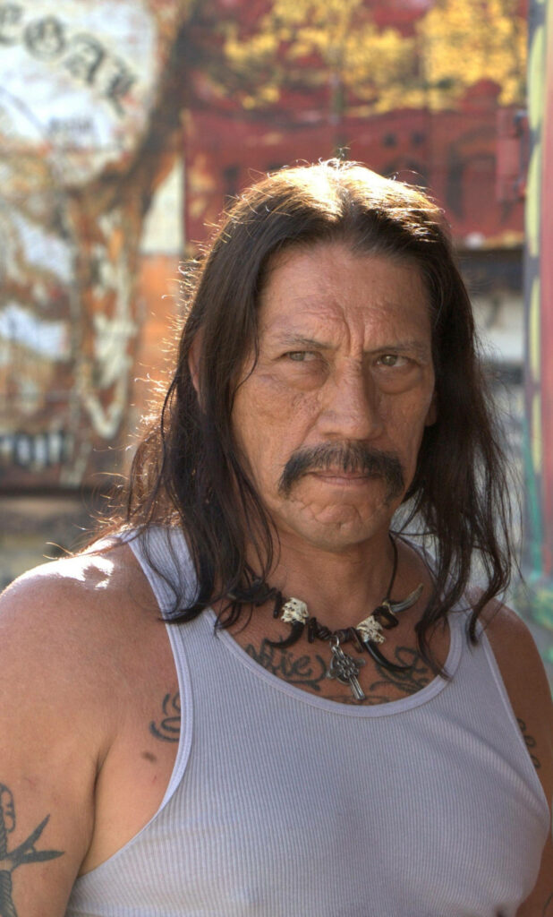 Danny Trejo in white tank top with tattoos and long hair intense rugged look wallpaper background