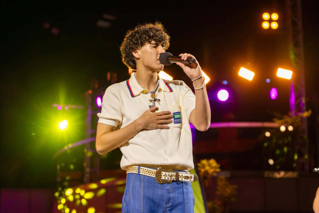 DannyLux singing on stage in white shirt and jeans with vibrant lights and lively crowd behind Wallpaper