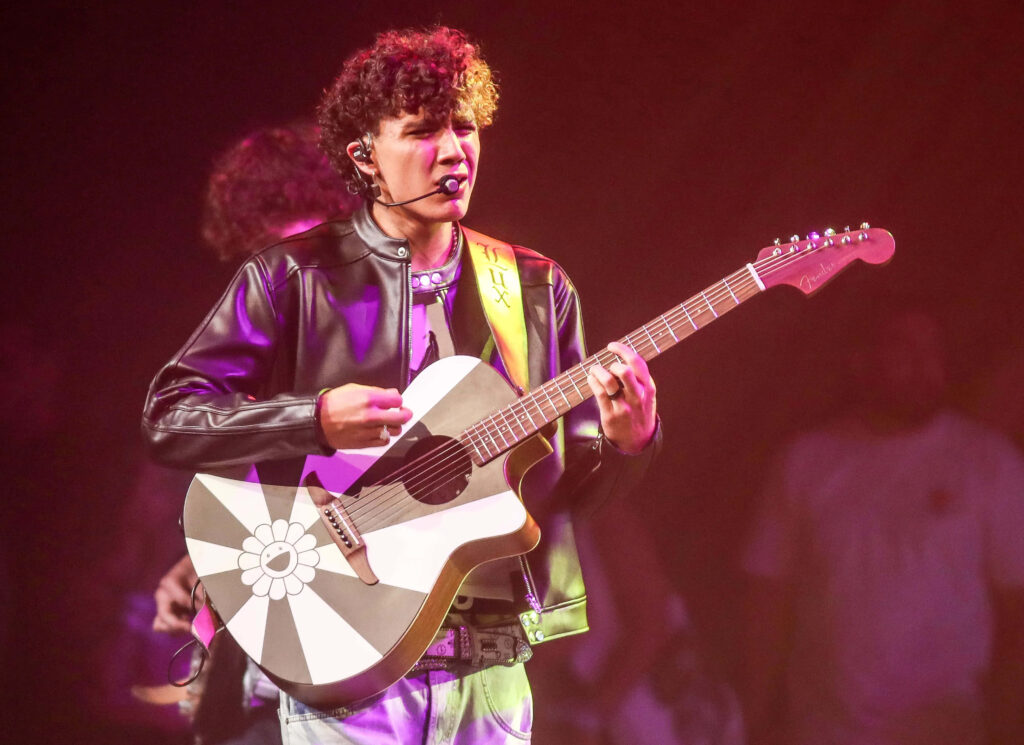 DannyLux performing live in black leather jacket playing flower design guitar vibrant concert lighting Wallpaper