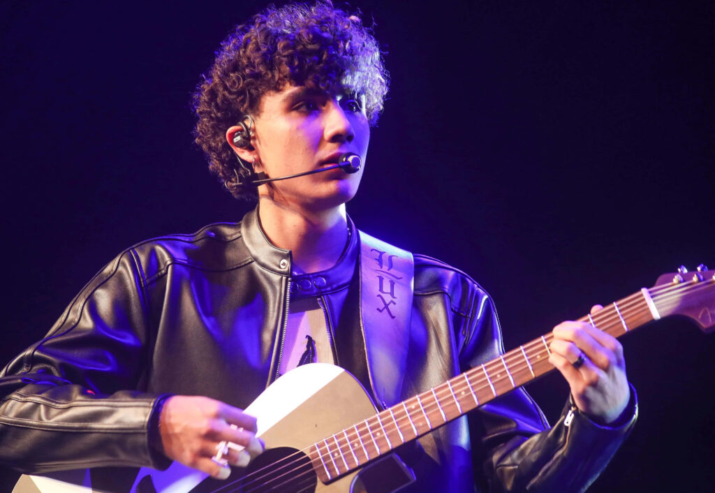 DannyLux performing live on stage with guitar vibrant lighting curly hair and leather jacket Wallpaper