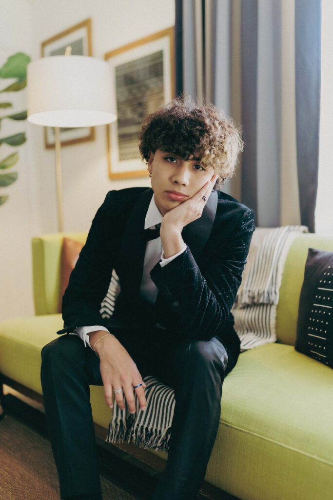 DannyLux relaxed on green sofa with curly hair modern decor soft natural light wallpaper background