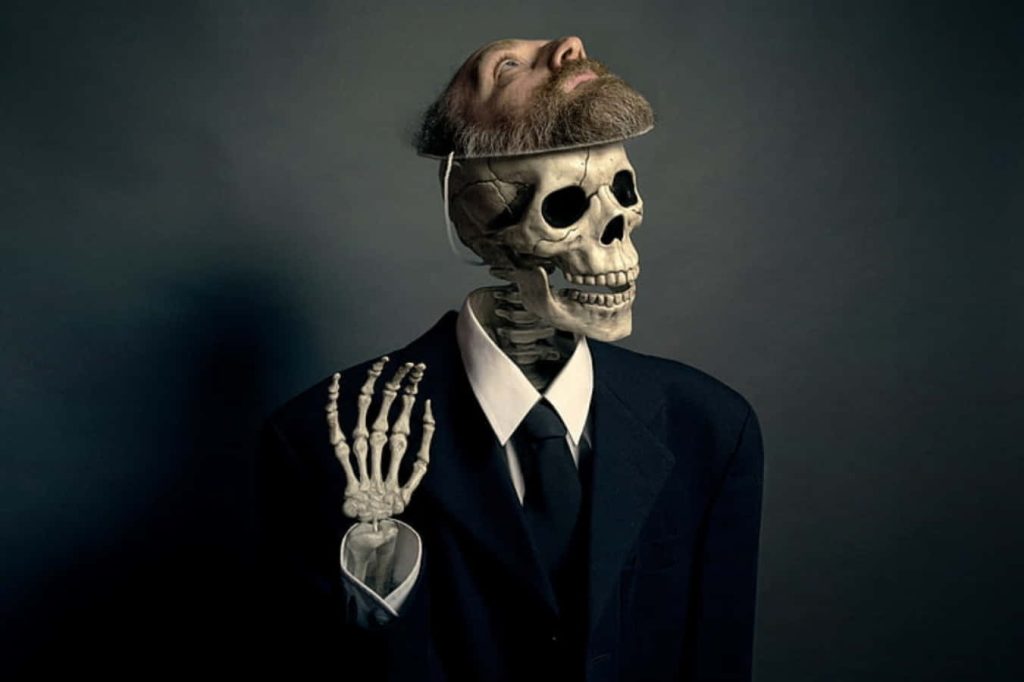 Dapper skeleton with bearded human face in dark suit and tie on moody artistic wallpaper background