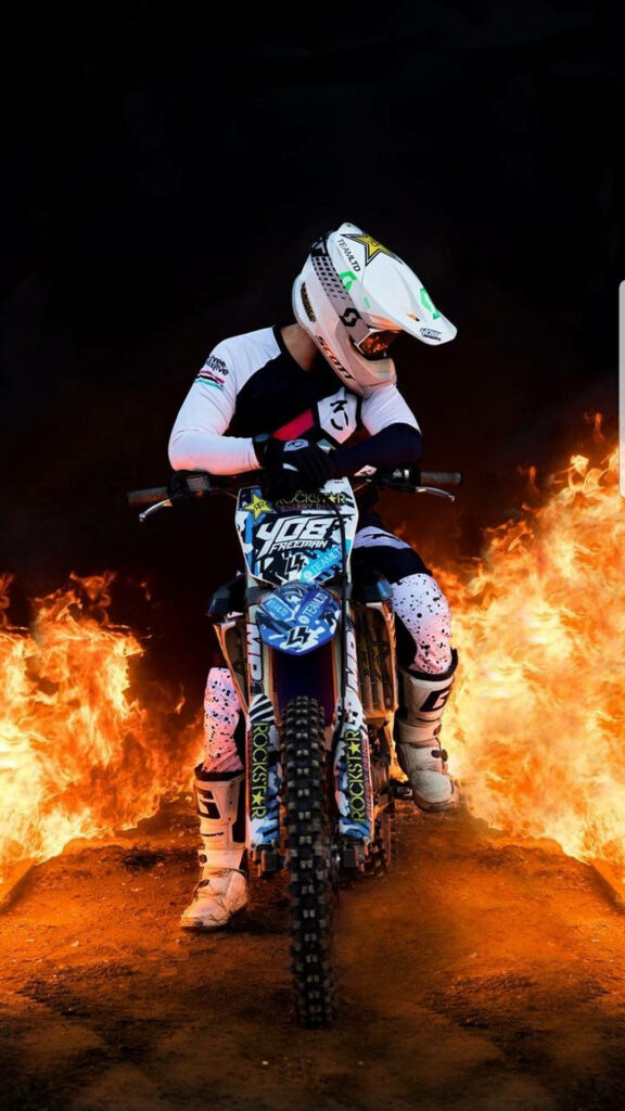 Daring motocross rider on blue white dirt bike with blazing flames dynamic intense wallpaper