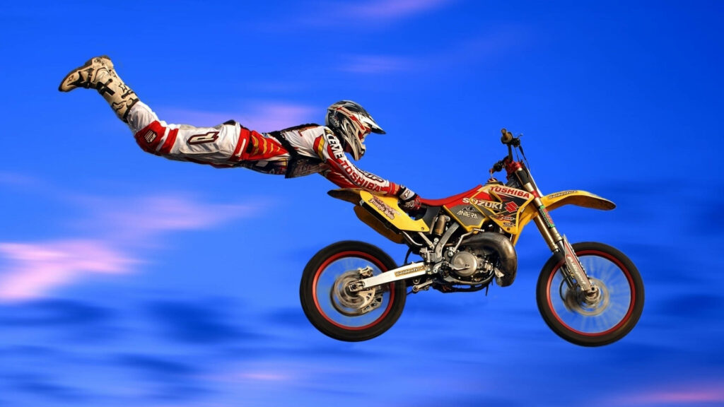 Motocross rider mid-air stunt on yellow Suzuki dirt bike blue sky pink clouds extreme sports Wallpaper