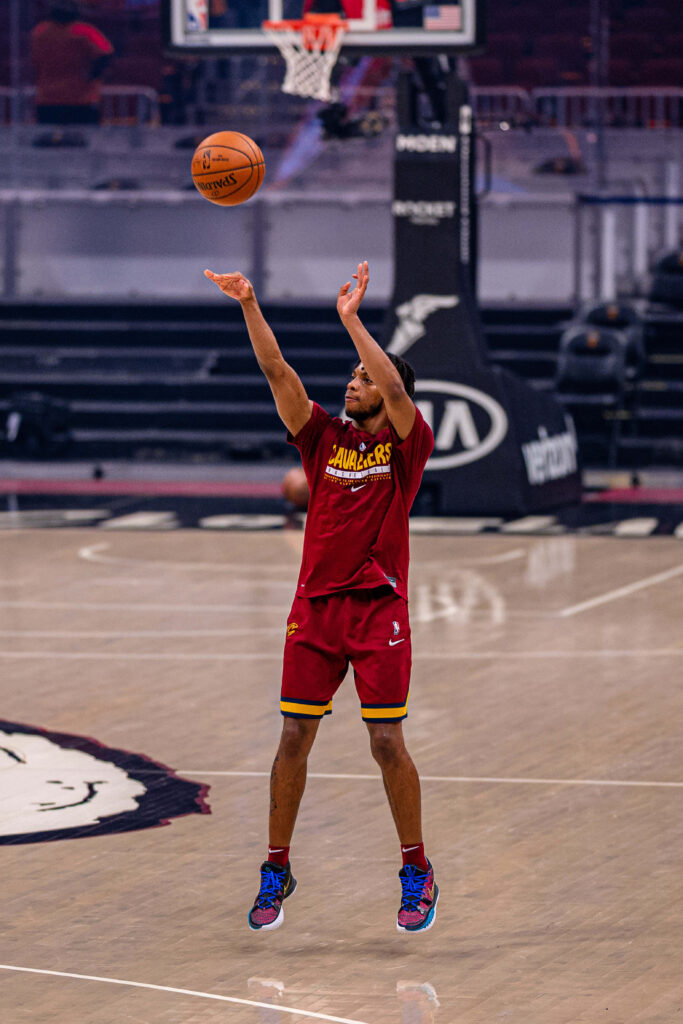 Darius Garland shooting basketball in Cavaliers uniform on polished court with warm arena light Wallpaper