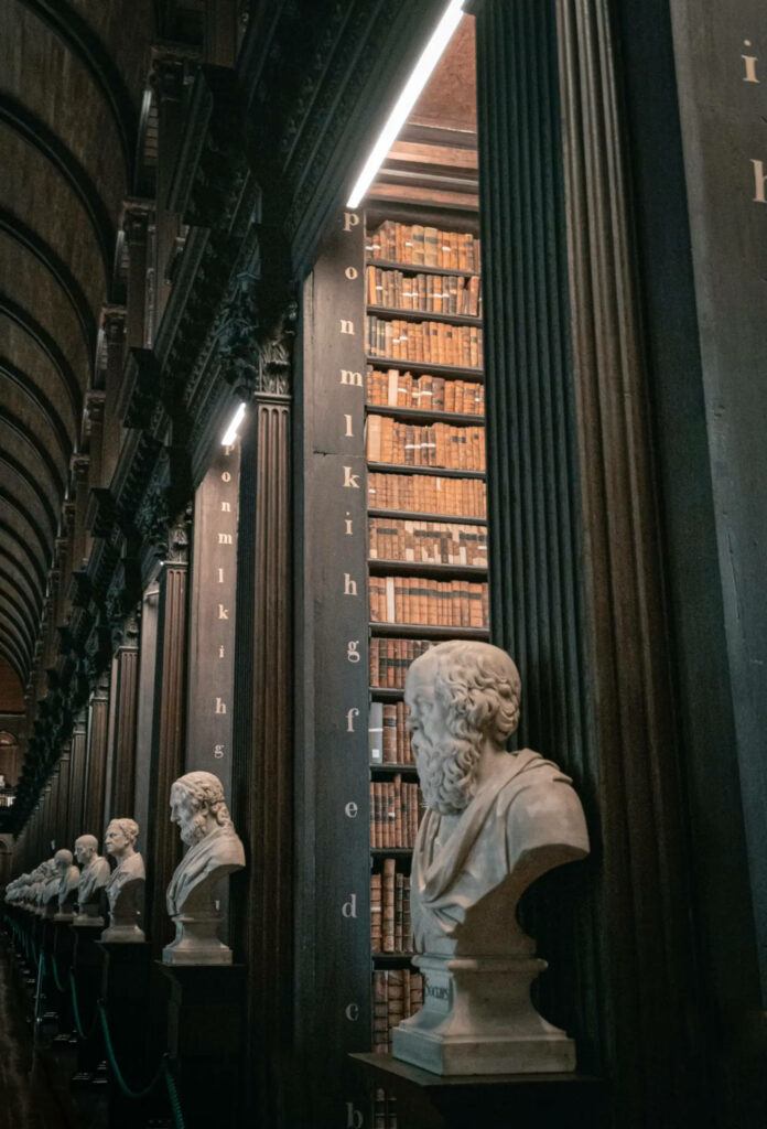 Dark academia library wallpaper with marble busts towering bookshelves classic columns moody lighting