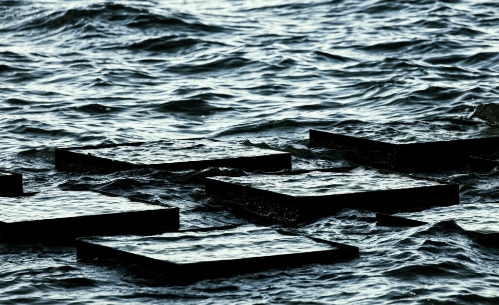 Dark choppy sea waves meet flat submerged plates blue gray tones minimalist wallpaper background