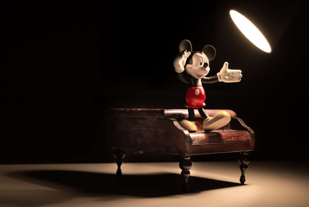 Classic Mickey Mouse figurine on miniature grand piano with dramatic spotlight dark background Wallpaper