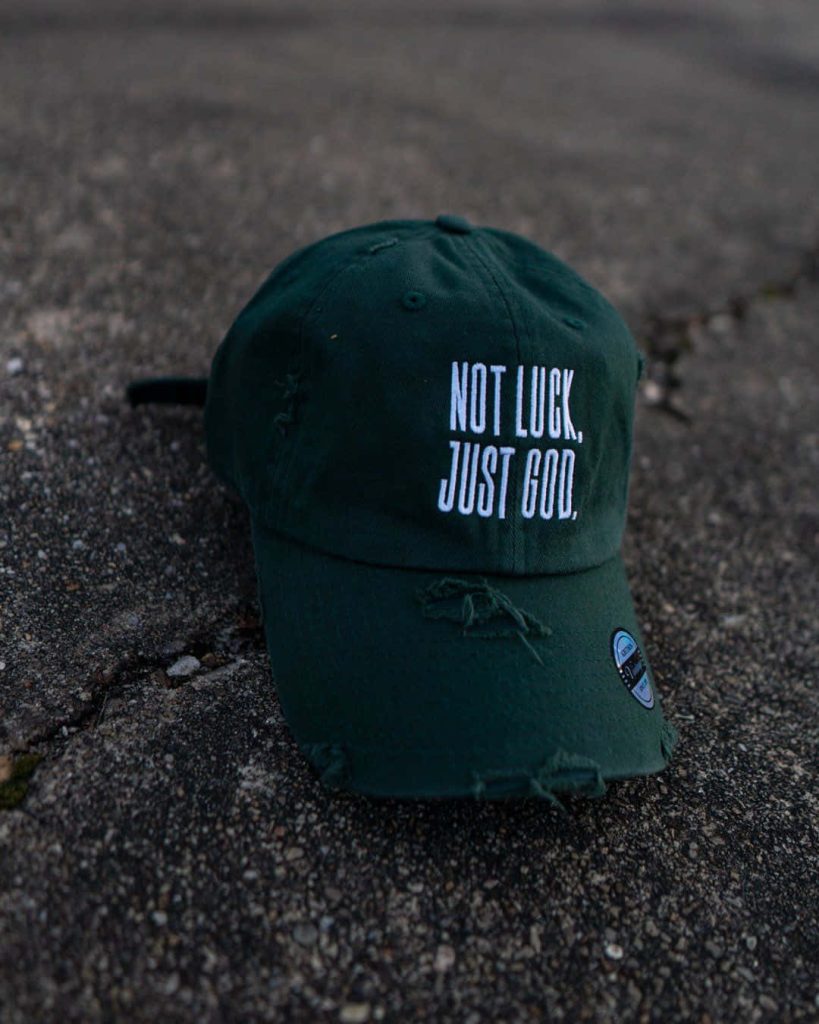 Dark green distressed baseball cap with white God quote embroidery on textured concrete background Wallpaper