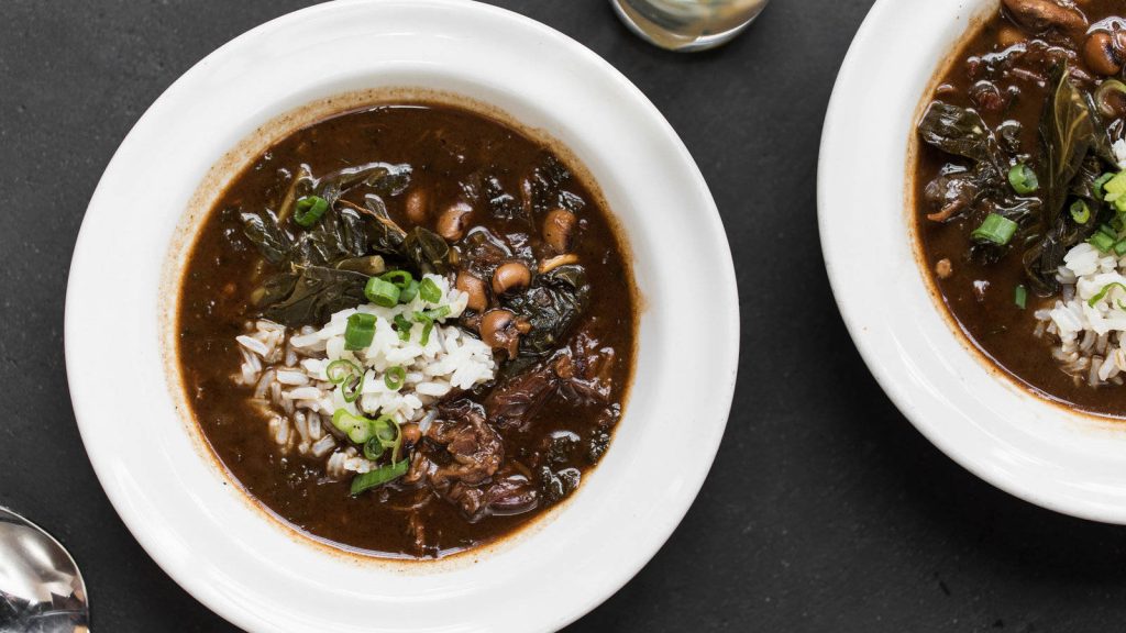 Top-down dark gumbo bowls over white rice garnished with spring onions and greens on black background Wallpaper