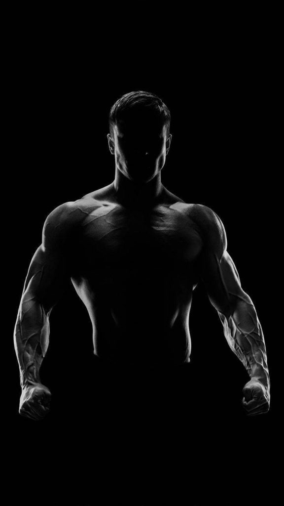 Muscular bodybuilder with high-contrast rim lighting showcasing shredded physique on black background Wallpaper