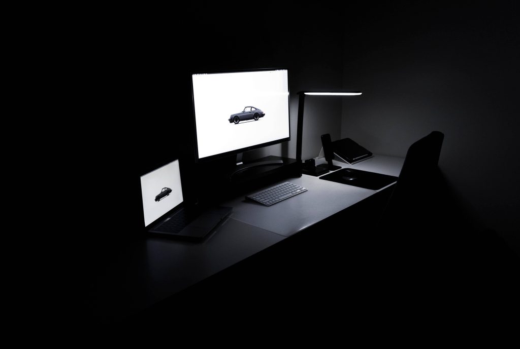Dark minimalist computer setup wallpaper with glowing Porsche 911 silhouette on screens