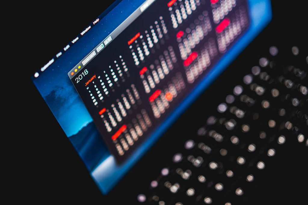 January 2018 calendar on dark mode laptop wallpaper with blurred keyboard and vibrant UI display