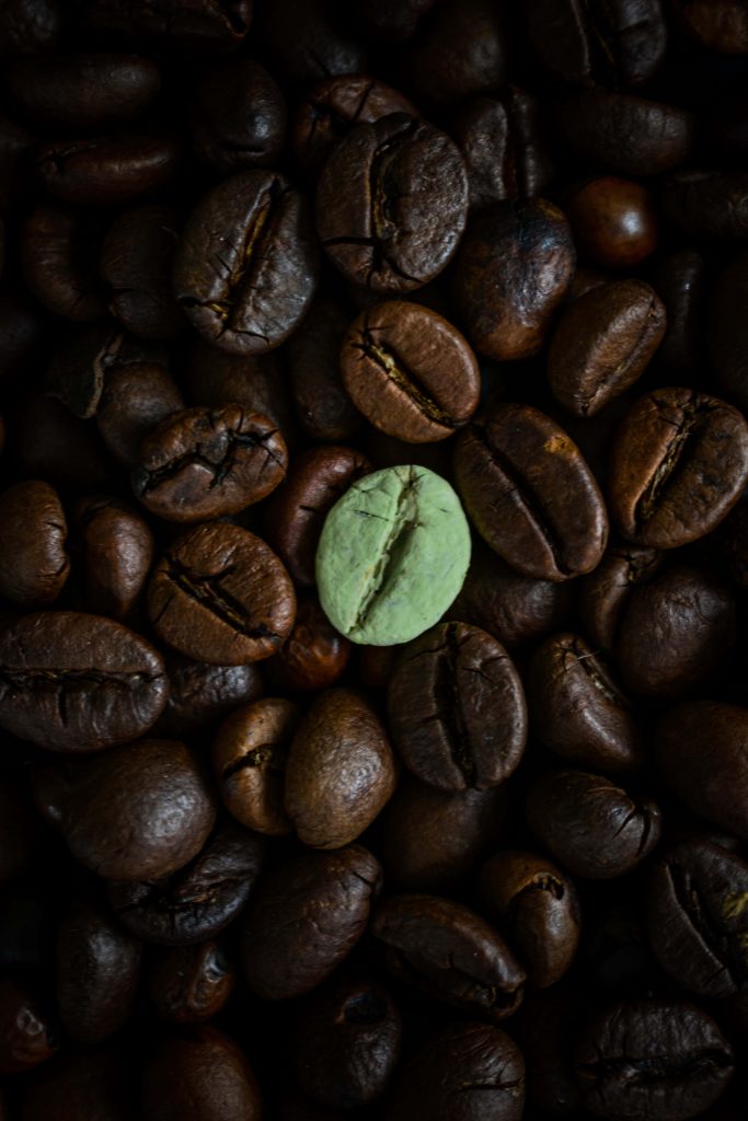 Macro shot of dark roasted coffee beans with a single green bean on moody background wallpaper